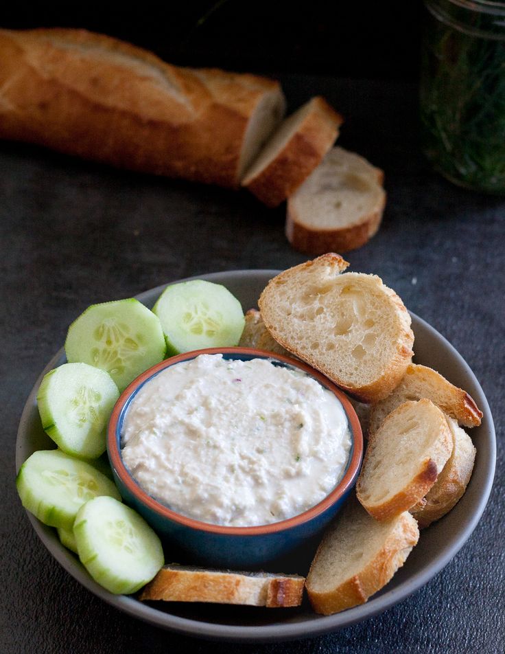 a plate with bread, cucumbers and dip on it