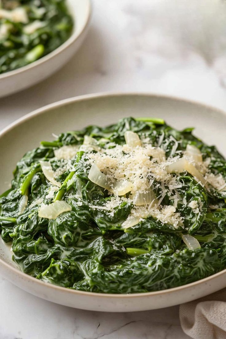 two bowls filled with spinach and cheese on top of a white table cloth next to each other