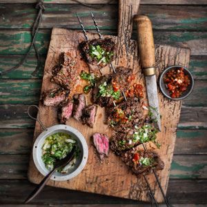 a wooden cutting board topped with meat and veggies next to a bowl of salsa