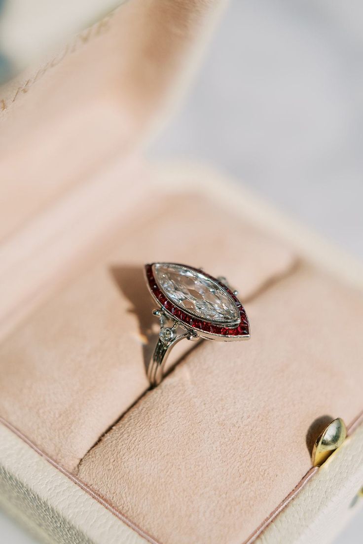 The Paltrow ring is a vintage ring in the Art Deco style. The ring centers a GIA-certified 1.54-carat Marquise cut diamond of H color, VS2 clarity. The stone is set in a platinum setting with a halo of 24 calibré cut rubies surrounding the center stone. A rose-cut diamond is bezel-set into each shoulder. The ring is currently size 6.5 and can be resized! Luxury Rose Cut Marquise Diamond Ring, Marquise Silver Ring, Luxury Marquise Ruby Ring With Diamonds, Art Deco Marquise Ring, Ruby Diamond Ring With Vvs Clarity And Baguette Cut, Marquise Emerald Diamond Ring With Brilliant Cut, Platinum Marquise Engagement Ring, Platinum Diamond Ring With Diamond Cut For Collectibles, Marquise Diamond Emerald Ring With Center Stone