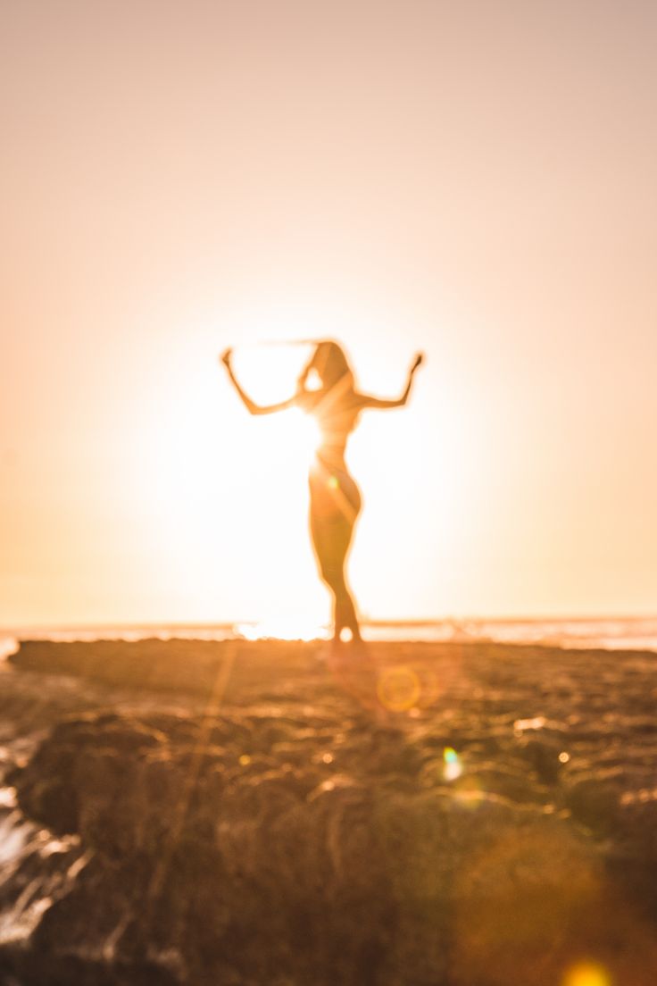 a woman standing on top of a sandy beach next to the ocean with her arms outstretched