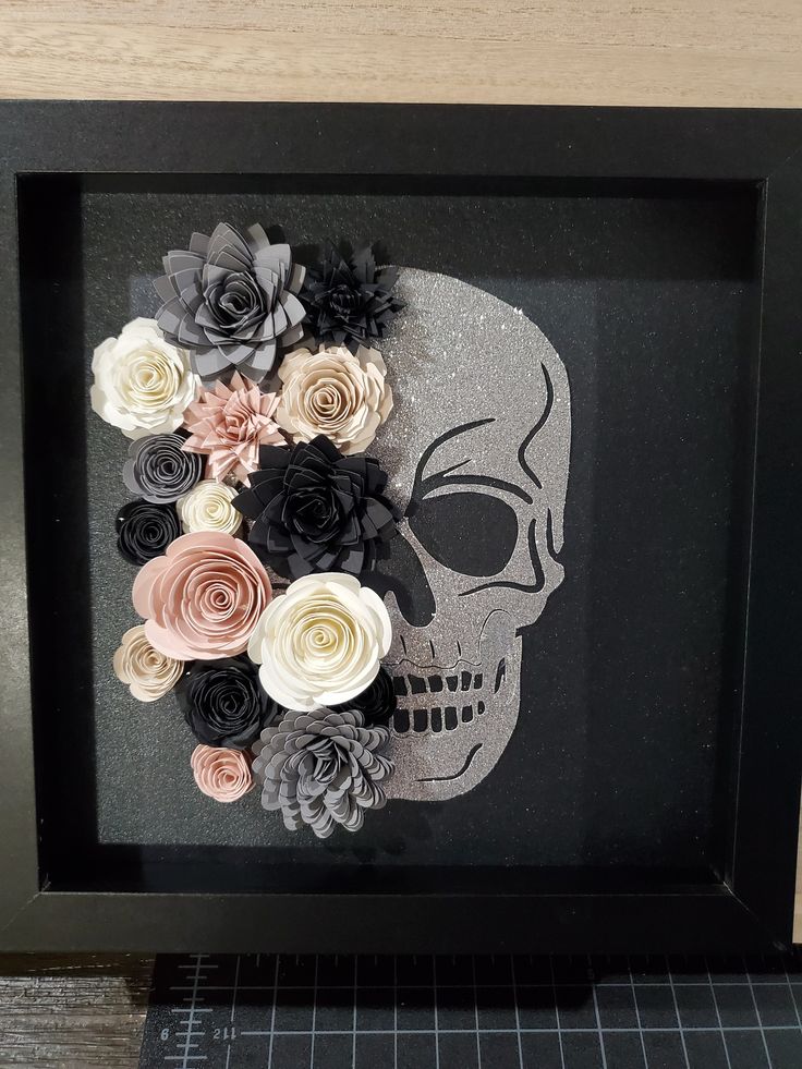 a shadow frame with paper flowers in the shape of a skull