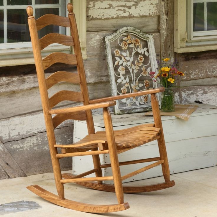 a wooden rocking chair sitting on top of a sidewalk next to a tree and window