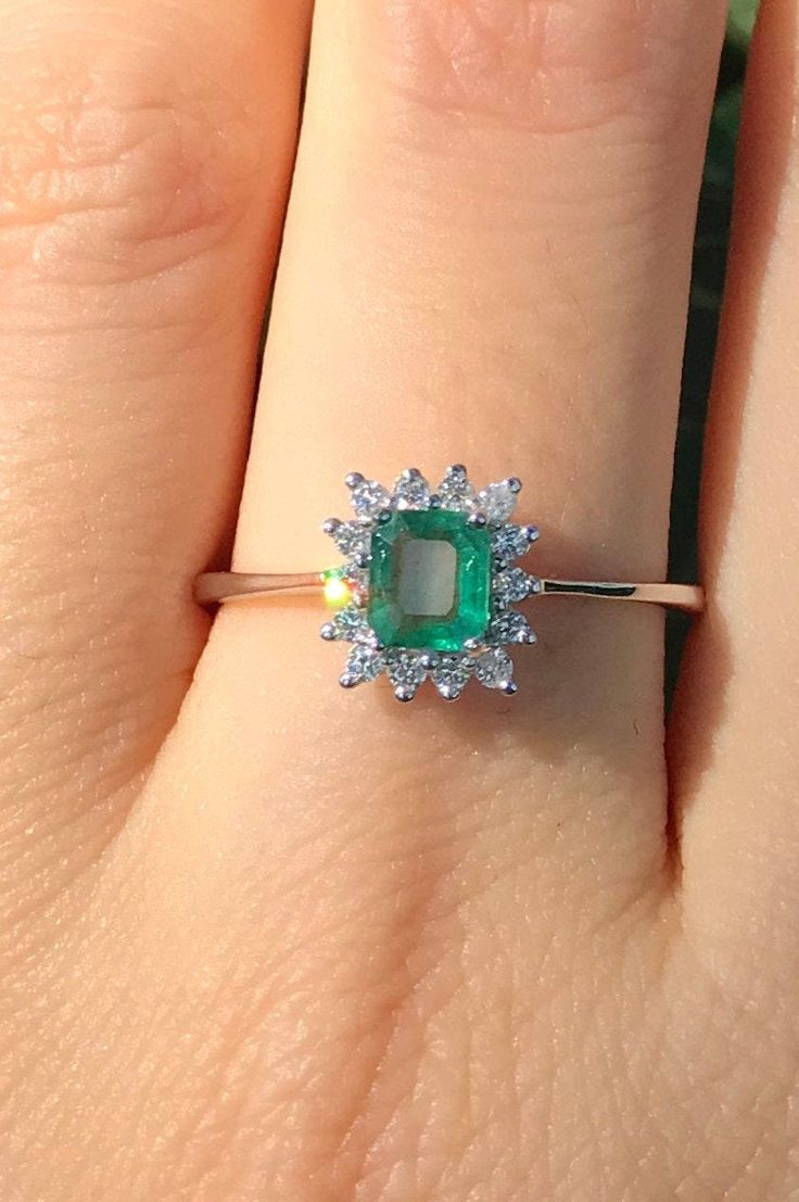 "A Dainty Promise/Engagement Ring for her features a faceted genuine 0.38ct Emerald adorned with a halo of petite genuine round diamonds handcrafted in 18k Solid White Gold is a one-of-a-kind ring. The shank is a tapered style. Wrapped in a box ready for gift-giving! Ring Info --------------------------------------- Genuine Emerald measure 5.5mm x 4.74mm, 0.38ct Sits off the finger 4.5mm Shank measure 1.7mm Petite Genuine White Diamond 18k White Gold For other sizes please convo me for a quote - Elegant Proposal Emerald Ring With Brilliant Cut, Radiant Cut Emerald Ring For Proposal, Formal Radiant Cut Ring With May Birthstone, Formal Radiant Cut May Birthstone Ring, Radiant Cut Diamond Emerald Promise Ring, Radiant Cut Diamond Ring For May Birthstone, May Birthstone Diamond Ring With Asscher Cut, Radiant Cut Rings With Center Stone For May Birthstone, Fine Jewelry Radiant Cut Emerald Anniversary Ring