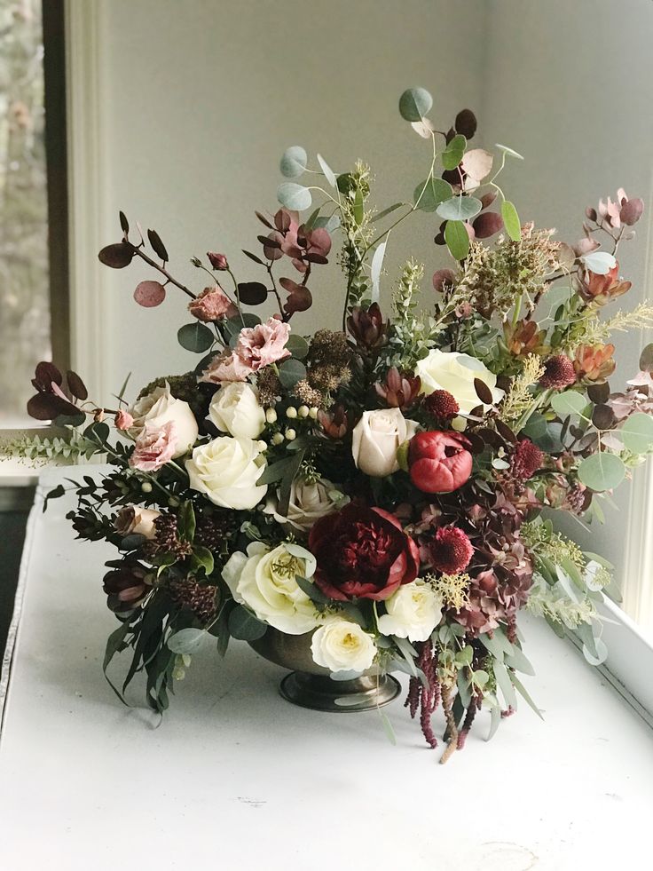 a vase filled with lots of flowers on top of a white table next to a window