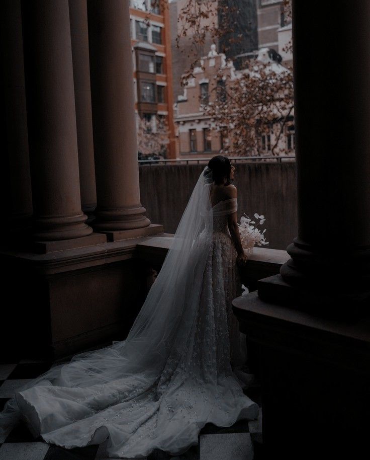 a woman in a wedding dress is standing by some pillars and looking out at the city