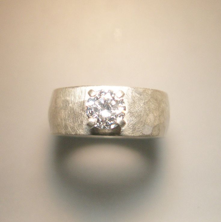 This is a ring with a substantial medium width and weight. It is set with a 6mm cubic zirconia which is aproximately the size of a 3/4 carat diamond. There is a gentle curve over the surface of the band. I first cast this piece, and then hand forge it. The forging, or hammer work actually hardens the metal. Because this ring is cast, there is no solder seam. The finish on this ring is brushed, but it can also be done in high polish. Available up to size 9 at this price. Please contact me for pri Wide Band Wedding Jewelry With Single Diamond, Modern Wide Band Ring With Brilliant Cut For Wedding, Diamond Ring With Tension Setting And Wide Band, Wide Band Diamond Ring With Tension Setting, Diamond Wedding Ring With Wide Band And Tension Setting, Modern Brilliant Cut Wide Band Wedding Ring, Modern Wide Band Wedding Ring With Round Cut, Diamond Wide Band Ring With Tension Setting For Wedding, Wedding Jewelry With Tension Setting And Wide Band