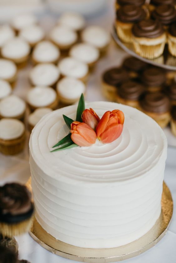 there is a white cake with two flowers on top and cupcakes in the background