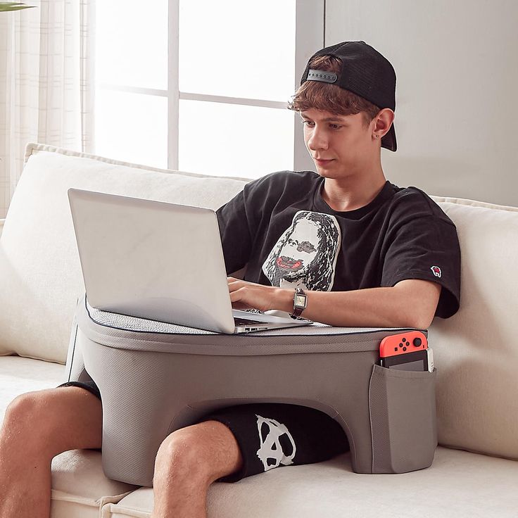 a young man sitting on a couch with a laptop and game controller in front of him