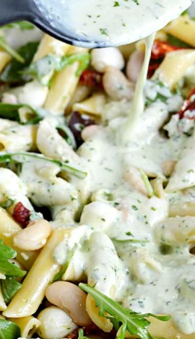 pasta salad with white sauce being drizzled over it