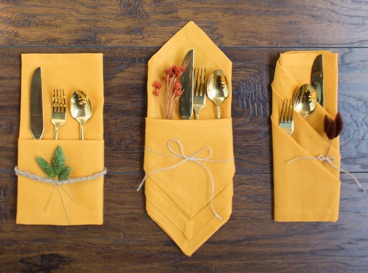 three napkins with forks, knives and spoons in them on a wooden table