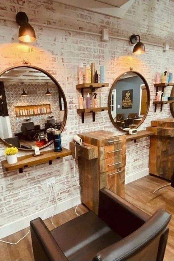 a hair salon with chairs and mirrors in front of brick wall, one chair is facing the mirror