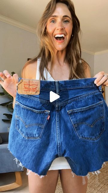 a woman holding up her jean shorts in front of her face and showing it to the camera