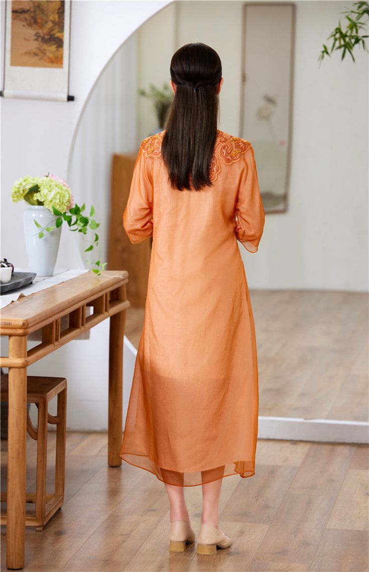 This elegant dress is a modern take on the traditional qipao (cheongsam), featuring a loose fit for comfort and style. The dress is crafted from a lightweight, semi-sheer fabric in a beautiful orange hue, perfect for both casual and formal occasions. Intricate Embroidery: The upper part of the dress is adorned with delicate embroidery, adding a touch of sophistication and artistry. Classic Mandarin Collar: The high, mandarin collar provides a classic and refined look. Asymmetrical Button Closure Luxury Spring Cheongsam With Mandarin Collar, Spring Embroidered Cheongsam With Stand Collar, Luxury Floral Embroidered Cheongsam With Mandarin Collar, Traditional Qipao, Luxury Red Cheongsam With Mandarin Collar, Red Qipao, Qipao Cheongsam, Qipao Dress, Delicate Embroidery