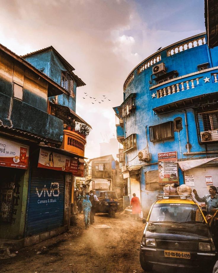 an old city street with cars parked on the side and people walking down the road