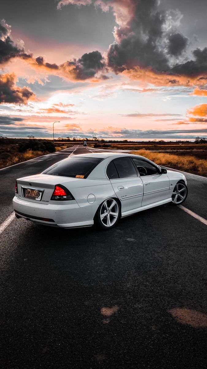 a white car is parked on the side of the road in front of an orange sunset