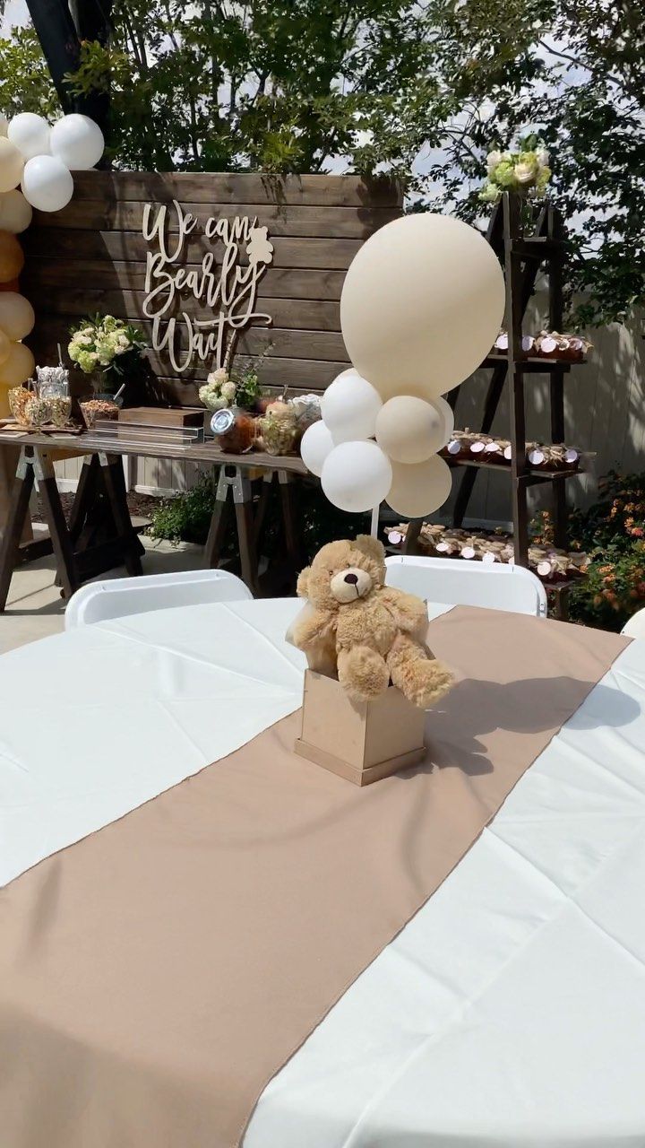 a teddy bear sitting on top of a table with balloons in the shape of letters