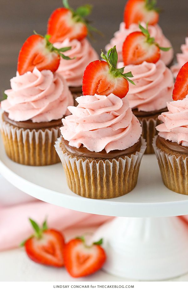 cupcakes with pink frosting and strawberries on top are sitting on a cake plate