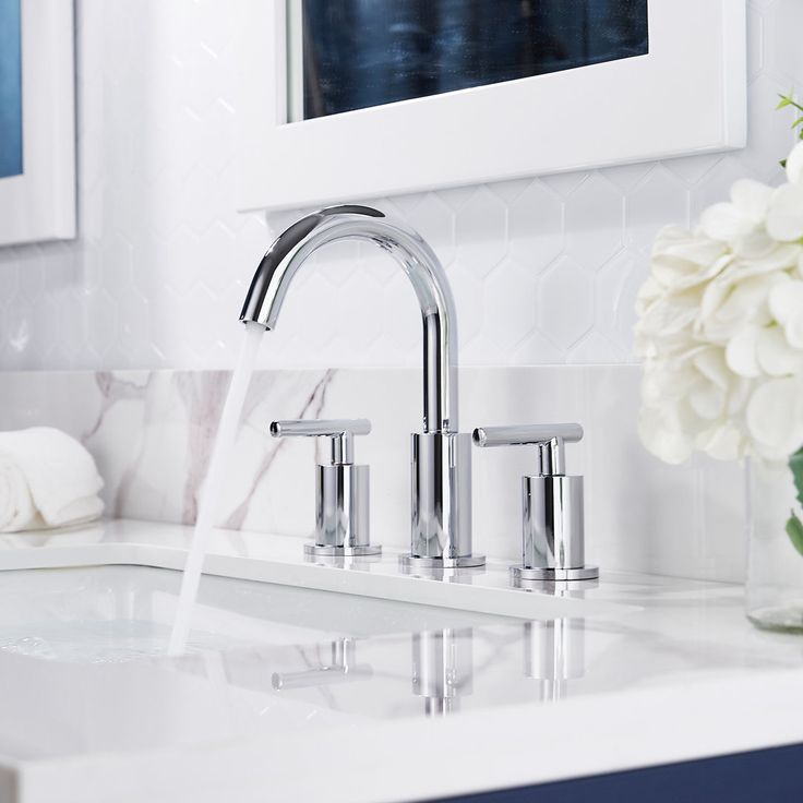 a bathroom sink with two faucets and white flowers in the vase next to it