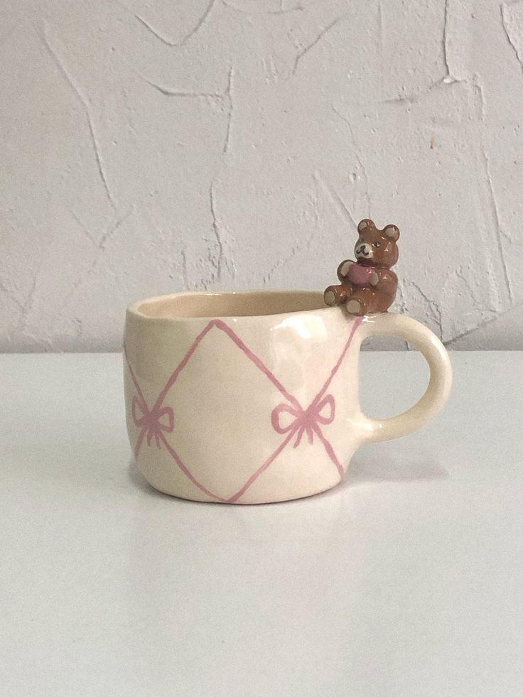 a ceramic cup with a teddy bear in the middle and pink bows on it's handle