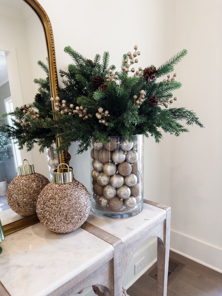 a vase filled with christmas decorations on top of a white table next to a mirror