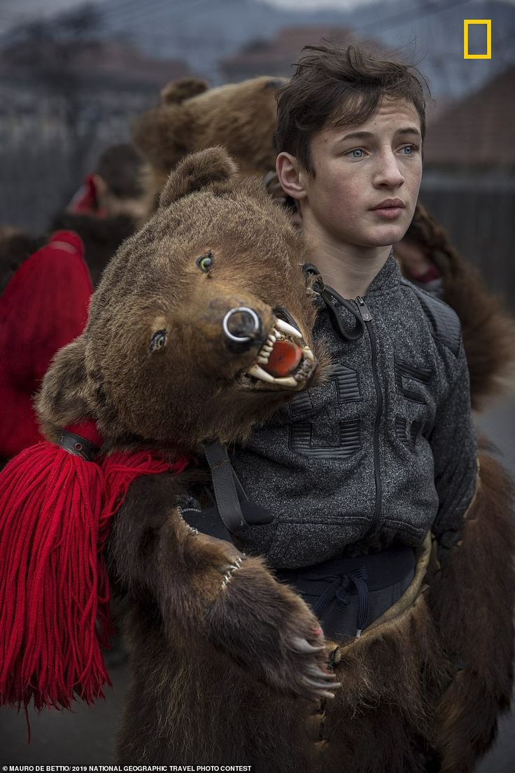 a young boy is carrying a stuffed bear on his back while other people are walking behind him