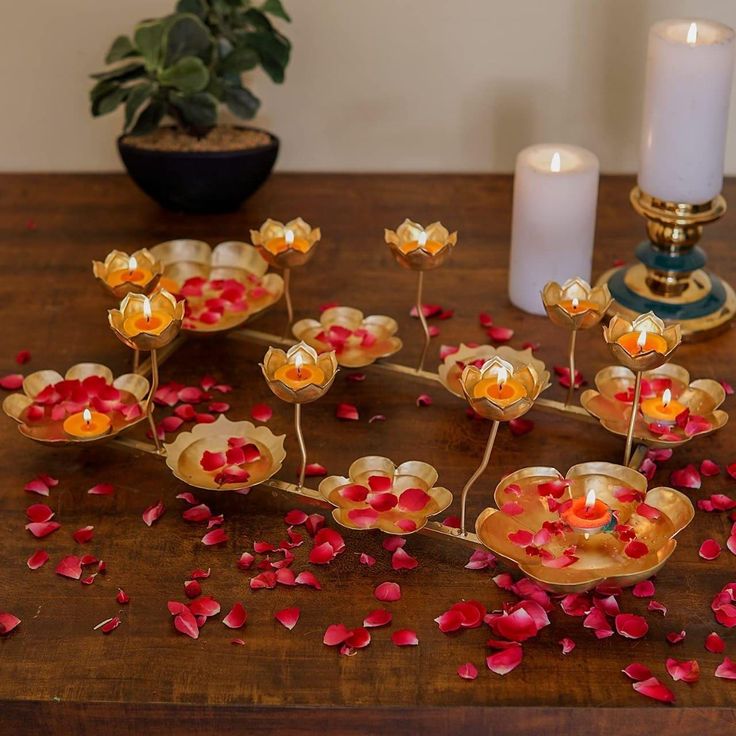 candles and petals on a wooden table with flowers in the center, next to a potted plant