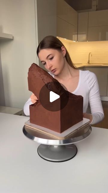 a woman sitting at a table in front of a cake with chocolate frosting on it