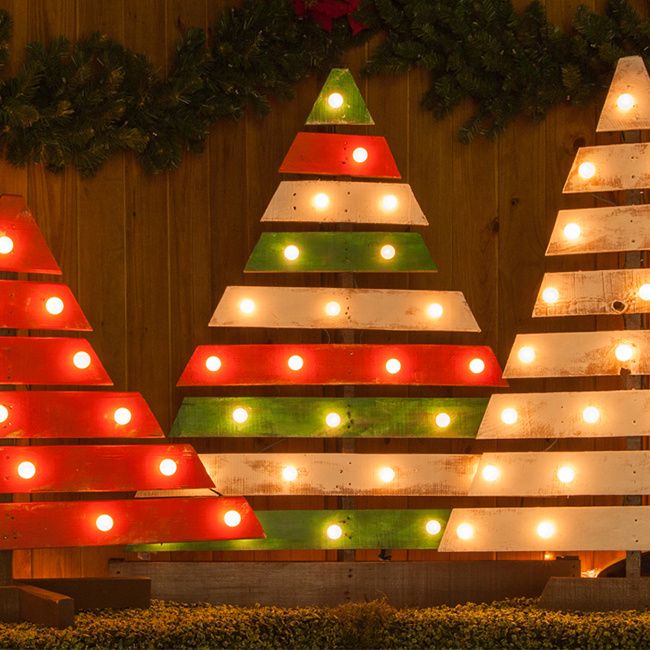 lighted christmas trees on display in front of a wooden wall