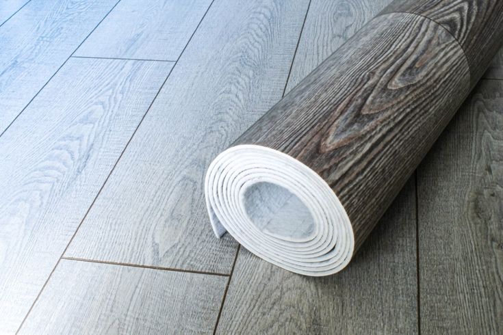 a roll of wood flooring sitting on top of a wooden floor next to a white rug