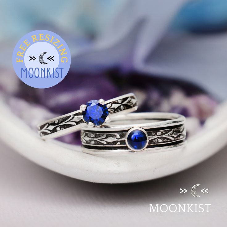 two silver rings with blue stones sitting on top of each other in front of a purple flower