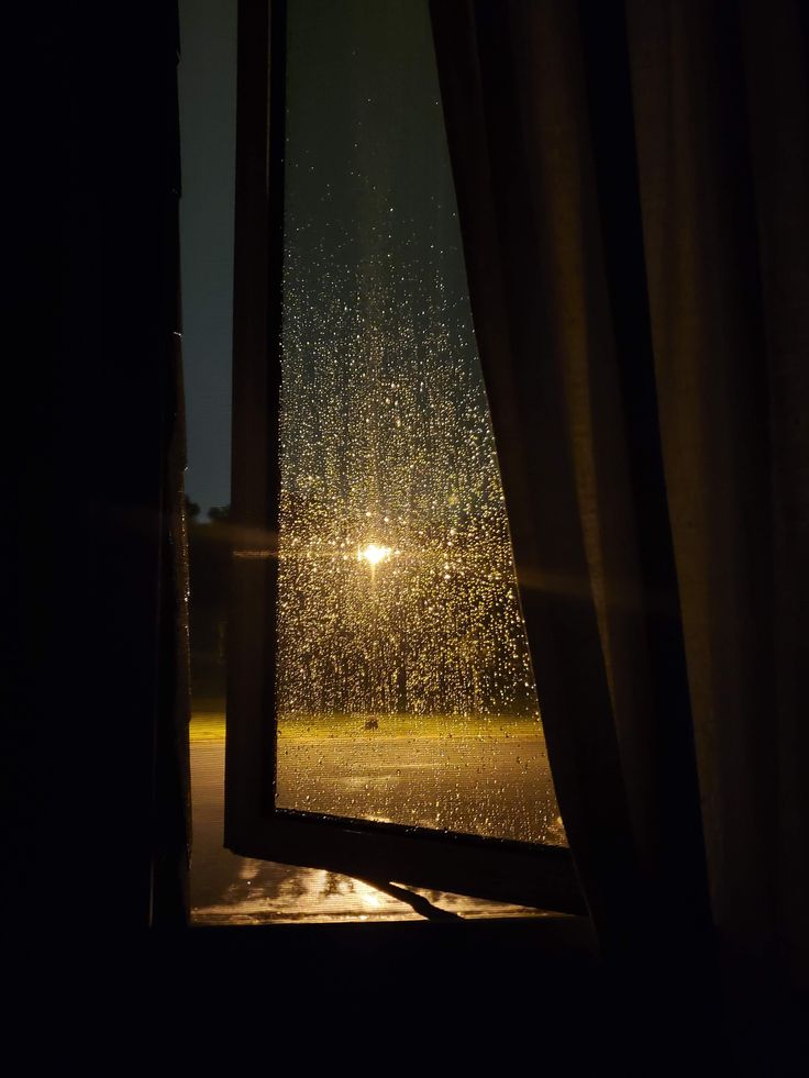 an open window with the sun shining through it and rain falling on the windowsill