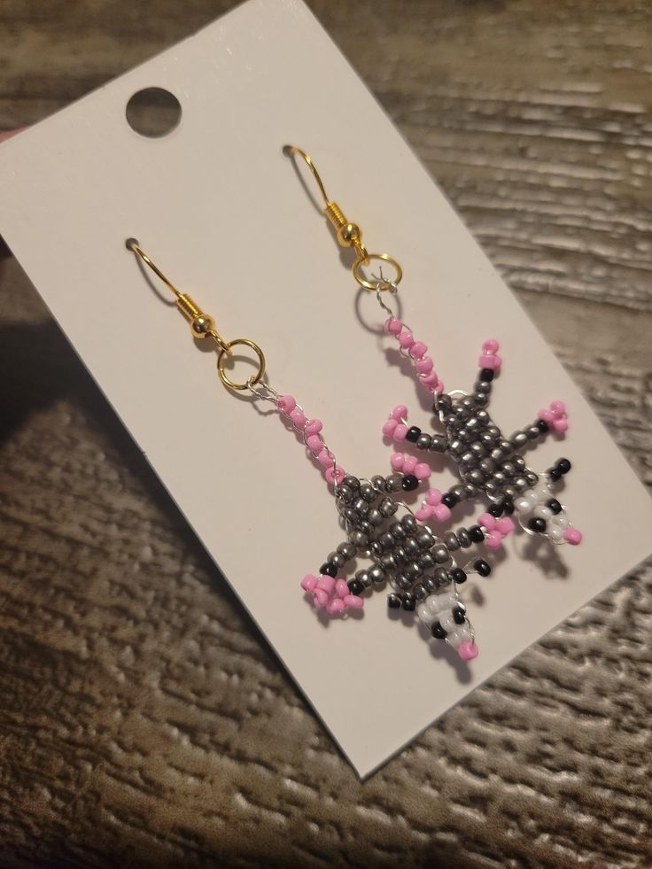 Add a touch of whimsy and nature-inspired elegance to your jewelry collection with our Possum Glam Beaded Dangle Earrings. Handcrafted with meticulous attention to detail, these earrings feature intricately beaded possum designs that dangle gracefully from your ears. Each pair is made with high-quality beads and hypoallergenic hooks, ensuring both beauty and comfort. Perfect for animal lovers and those who appreciate unique, artisanal accessories, these earrings are a delightful addition to any outfit. Whether you're dressing up for a special occasion or adding a playful twist to your everyday look, our Possum Glam Beaded Dangle Earrings are sure to make a statement. Details: *Handmade with love and care *Lightweight and comfortable for all-day wear *Hypoallergenic hooks *Length: [Insert l Whimsical Beaded Dangle Jewelry, Whimsical Adjustable Beaded Earrings, Whimsical Beaded Earrings With Dangling Beads For Gifts, Whimsical Adjustable Beaded Dangle Earrings, Whimsical Beaded Earrings As A Gift, Unique Flower Drop Earrings With Dangling Beads, Whimsical Handmade Beaded Dangle Earrings, Handmade Whimsical Beaded Drop Earrings, Whimsical Handmade Beaded Drop Earrings