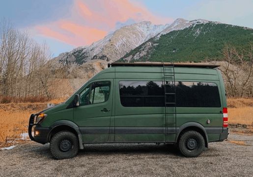 a green van parked on top of a dirt field next to a mountain covered in snow