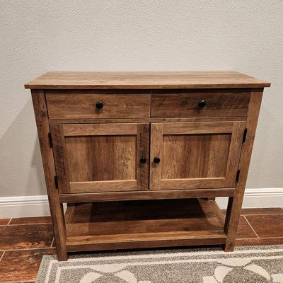 a wooden cabinet sitting on top of a tile floor next to a white wall and rug