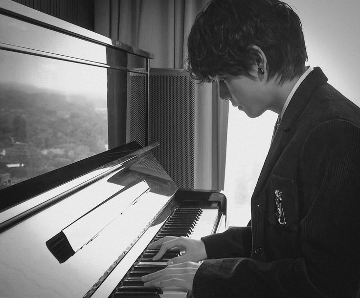 a young man playing the piano in front of a window