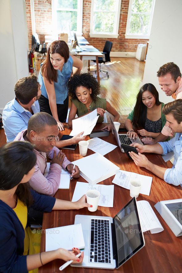 a group of people sitting around a table with laptops and papers on the table