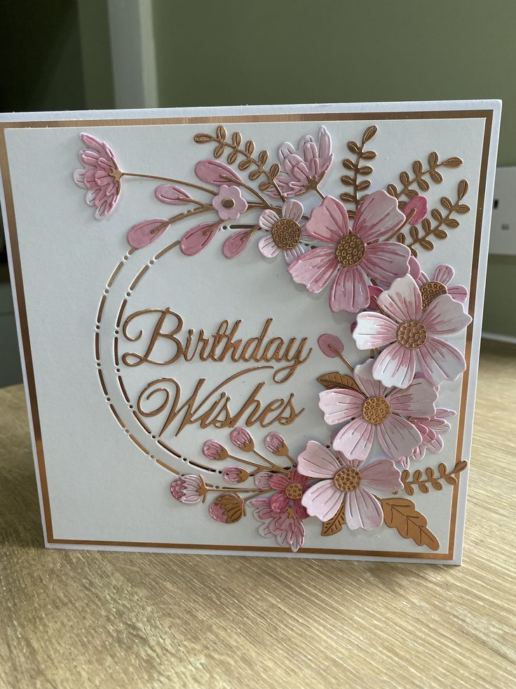 a handmade birthday card with pink flowers and gold foil on the front, sitting on a table