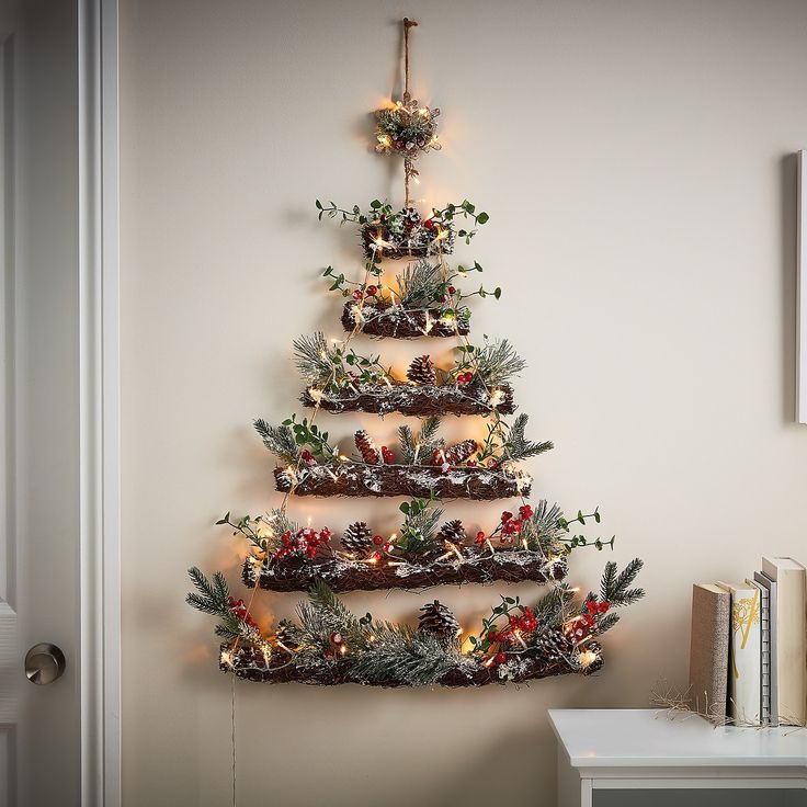 a christmas tree made out of branches and pine cones with lights on it is hanging from the wall