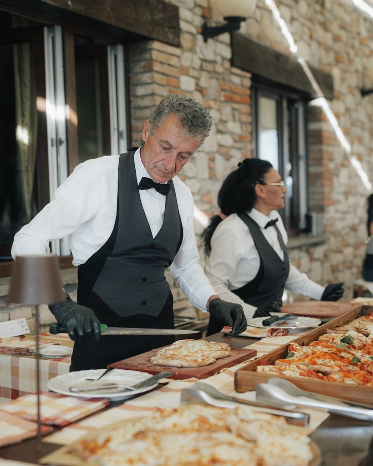 a man in an apron preparing pizzas at a table with other people behind him