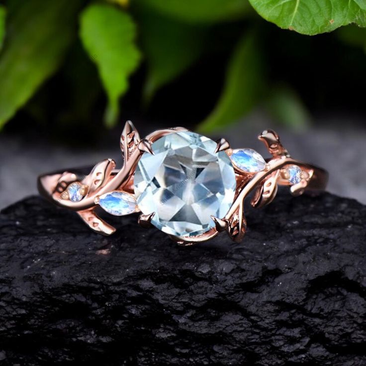 a ring with an aqua blue stone surrounded by leaves on top of a black rock