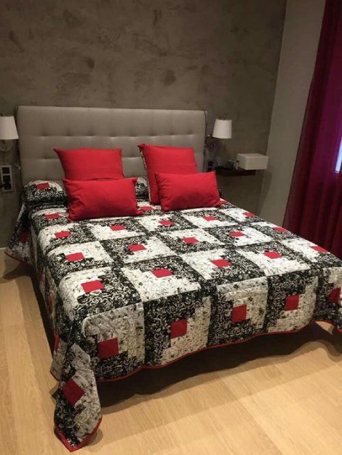 a bed with two red pillows on top of it next to a night stand and lamp