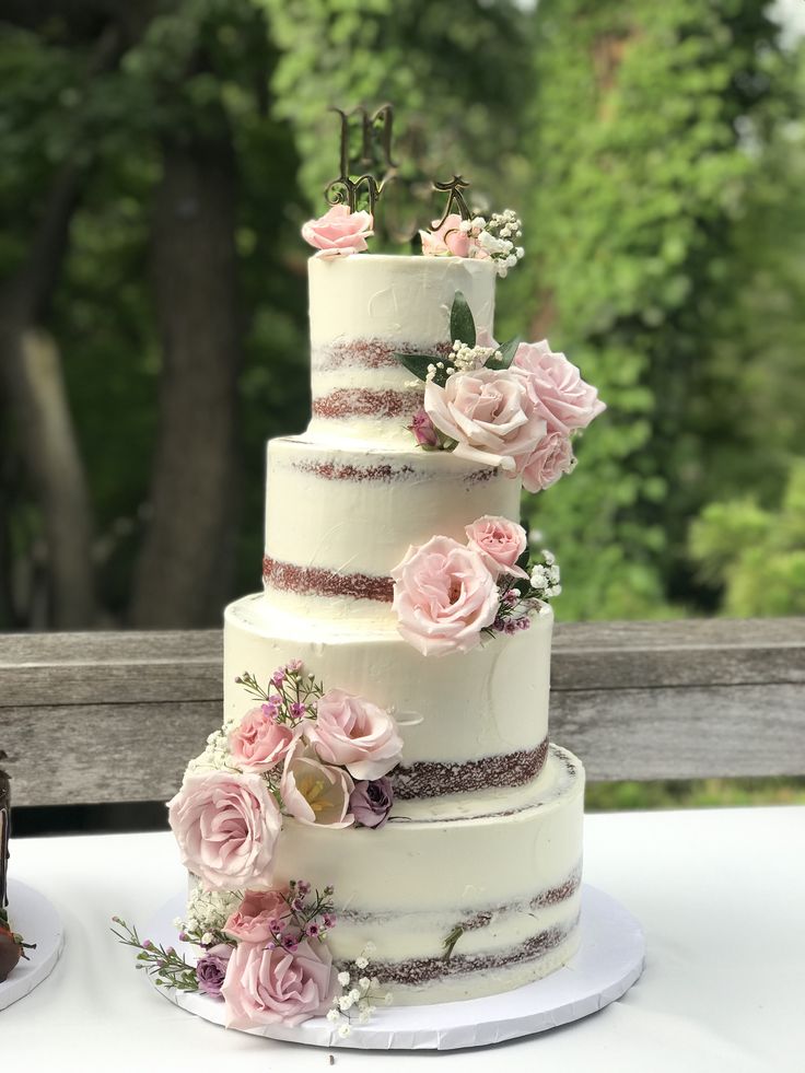 a three tiered wedding cake with pink flowers on the top and bottom, sitting on a table outside