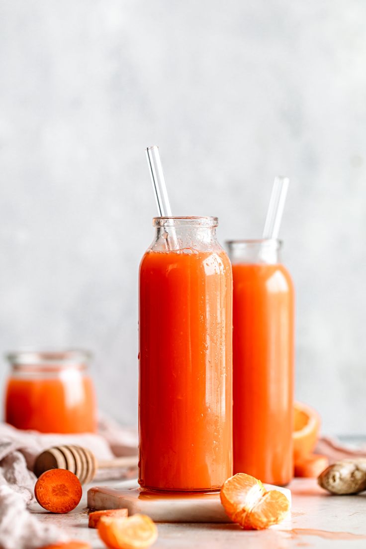 two glasses filled with orange juice on top of a table next to sliced carrots