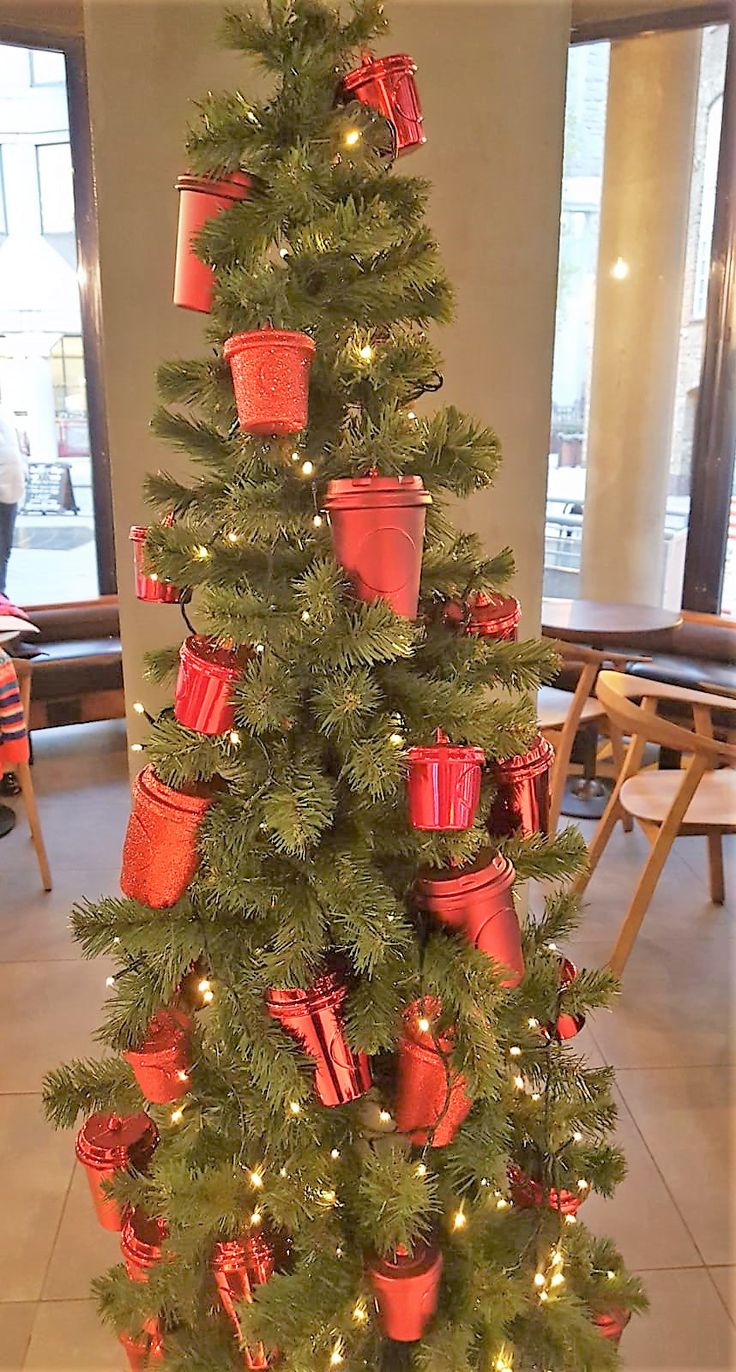 a small christmas tree with red pots and lights on it's branches in a lobby