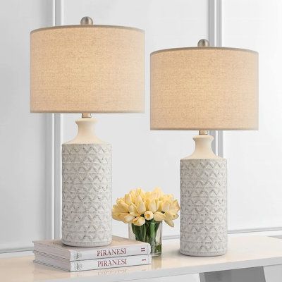 two white vases with yellow flowers sit on a table next to books and a lamp