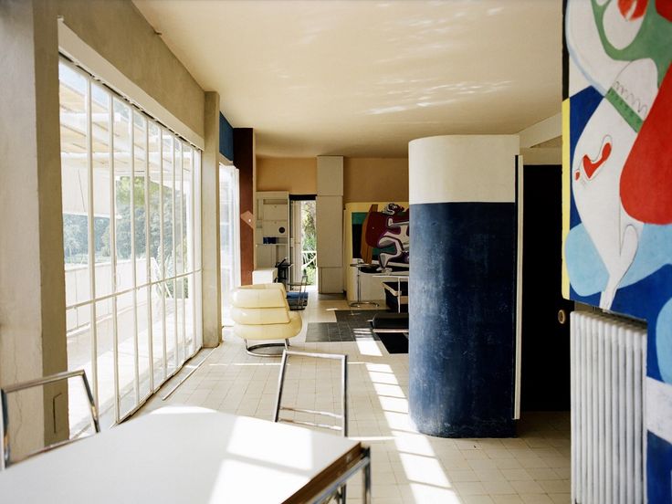 an empty room with chairs and paintings on the wall, in front of large windows