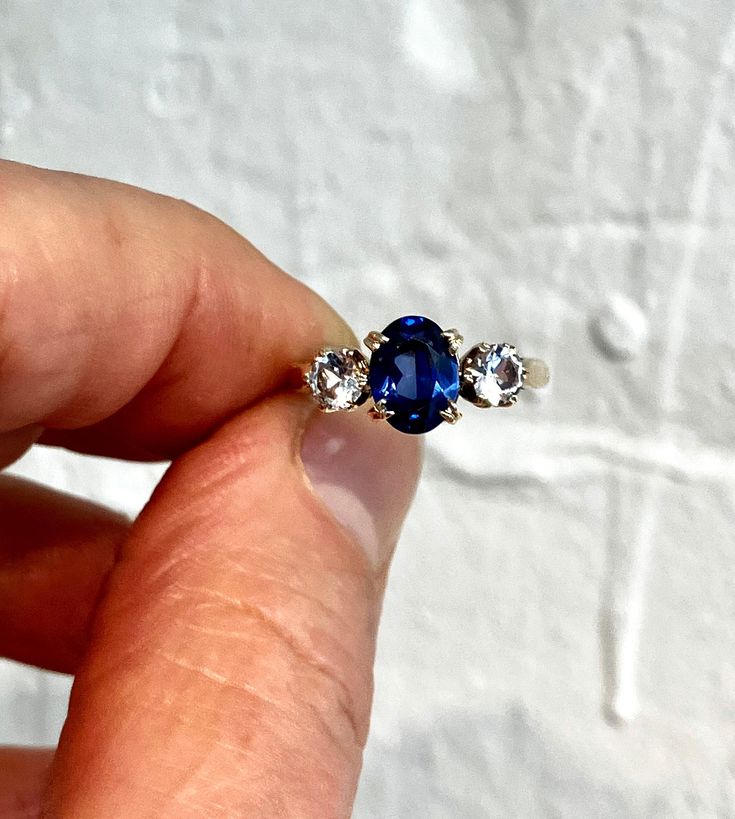 Lab grown sapphire and white spinel 9ct solid gold trilogy ring. This blue stone does test as sapphire, but I think it's more likely to be lab grown, but looks absolutely amazing. CONGRATS: Excellent  CENTRE STONE SIZE: 8mm x 6mm ( 1.8 carat ) CURRENT FINGER SIZE: UK size L. Can be altered to the sizes on the drop down menu. WEIGHT: 2.7g This ring has been professionally checked, cleaned and polished. Comes in a new box. Timeless Hallmarked Sapphire Ring, Timeless Sapphire Ring With Birthstone, Timeless Sapphire Birthstone Ring, Three-stone Lab-created Sapphire Ring, Three Stone Lab-created Sapphire Ring, Three Stone Sapphire Round Ring Fine Jewelry, Sapphire Three Stone Diamond Ring, Sapphire Three Stone Round Cut Diamond Ring, Three Stone Sapphire Diamond Ring With Round Cut