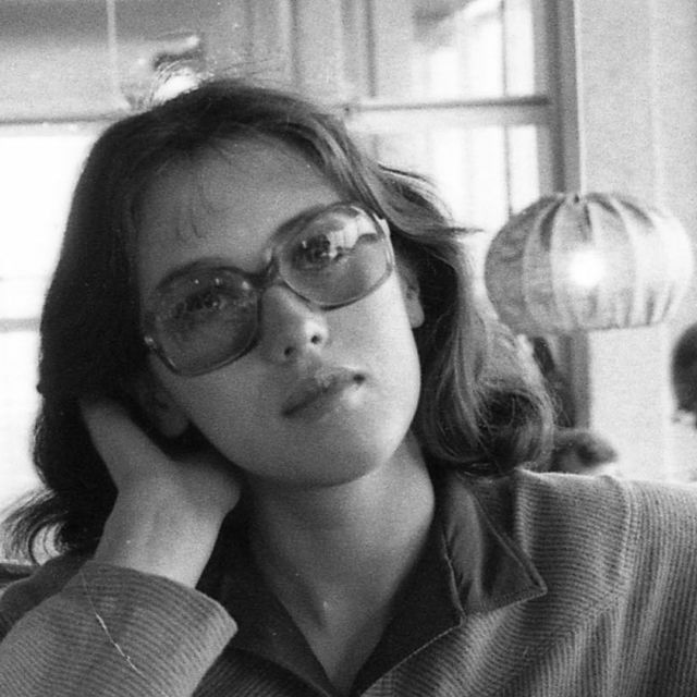 black and white photograph of a woman with glasses looking off to the side while holding her hand near her face