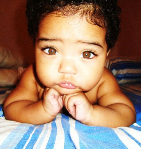 a little boy laying on top of a bed with his hands under his chin and looking at the camera